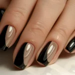 A hand displaying a variation of a French manicure with glossy black/beige base and black tips swept diagonally.