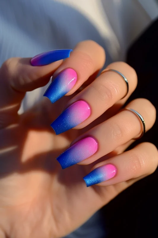 Square-shaped nails with a pink to blue ombre and glitter.