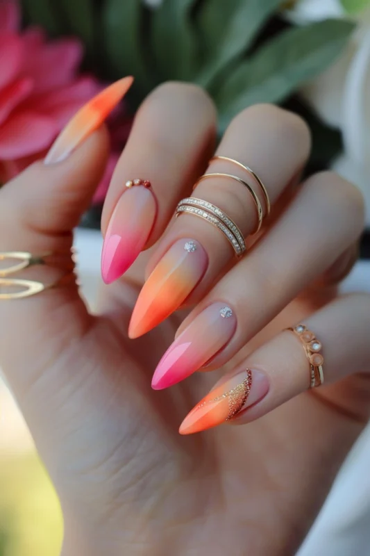 Stiletto nails with pink and orange ombre and rhinestones.