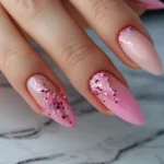 Elegant long almond-shaped nails in pretty pink nail polish adorned with glitter accents.