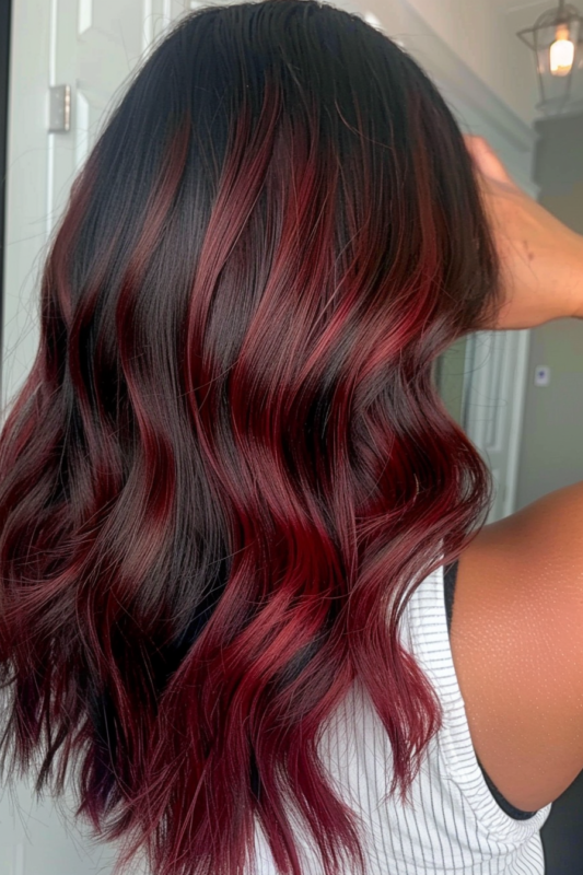 Back view of long black hair with a garnet red balayage, styled in loose waves.