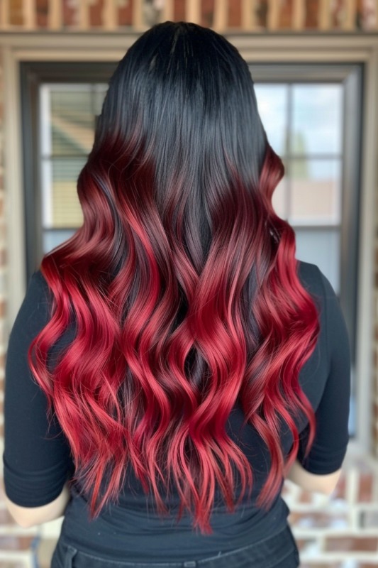 Back view of long black hair with a vivid ruby red ombre, styled in loose waves.