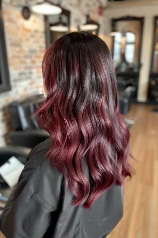Woman with wavy black hair and subtle burgundy balayage.