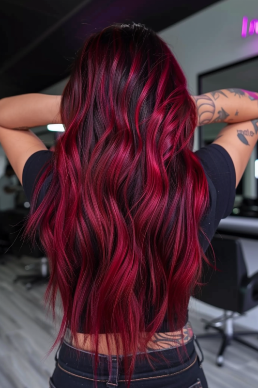 Long, wavy black hair with magenta red balayage highlights.