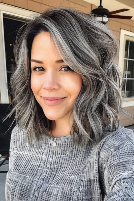 Woman with a vibrant salt and pepper hairstyle, featuring voluminous waves and a blend of silver and darker shades.
