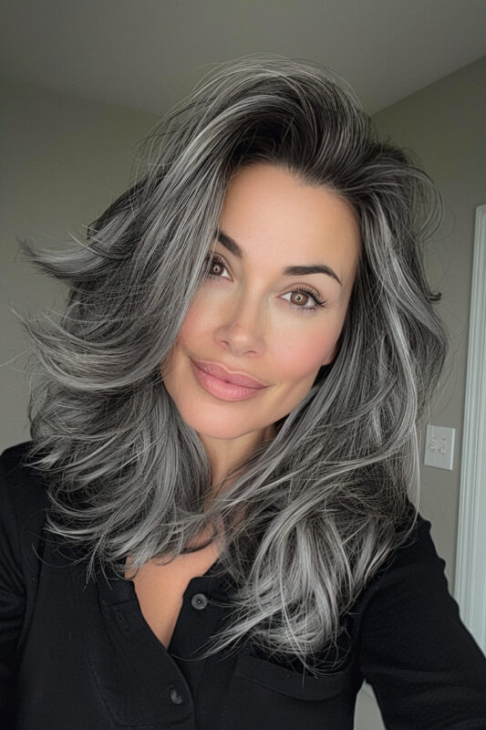 Woman with modern salt and pepper hair, featuring voluminous layers and natural gray streaks on a dark base.