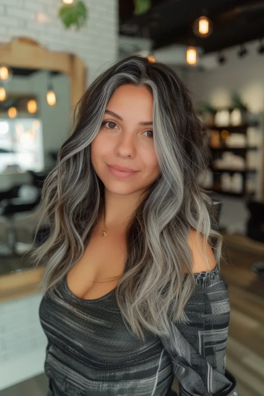 Woman with dark brown hair and grey/silver highlights, styled in soft waves.