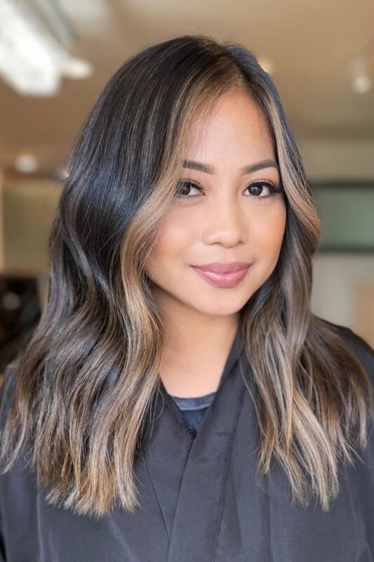 Woman with a honey blonde money piece and soft balayage on black hair.