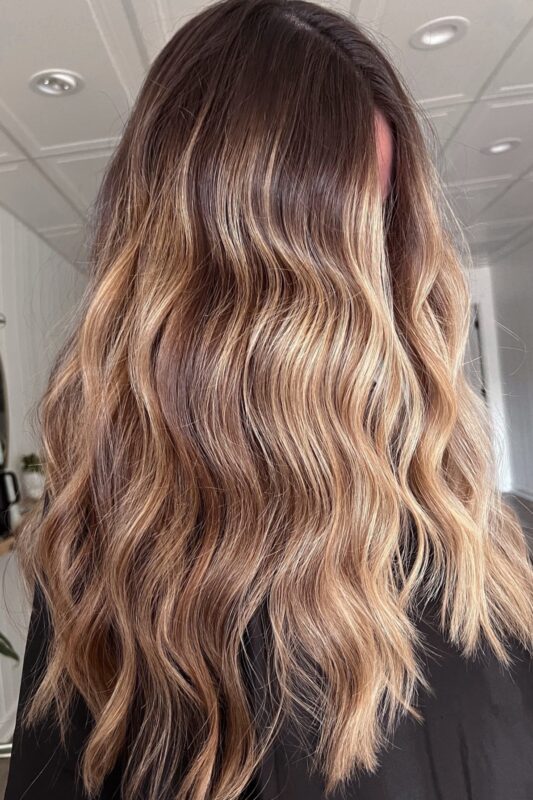 Woman with bright warm blonde balayage on dark warm brunette hair.