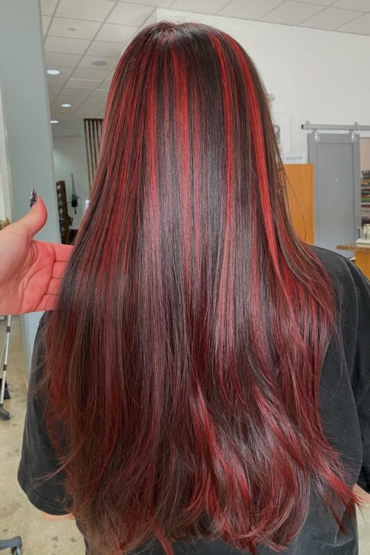 Woman with wavy brown hair and vibrant red highlights.