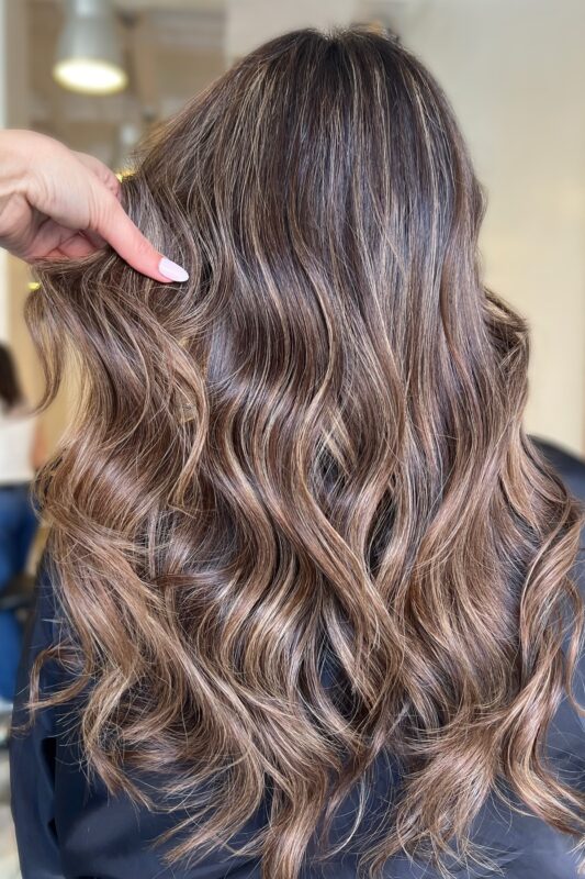 Mujer con cabello castaño chocolate y balayage rubio cálido.