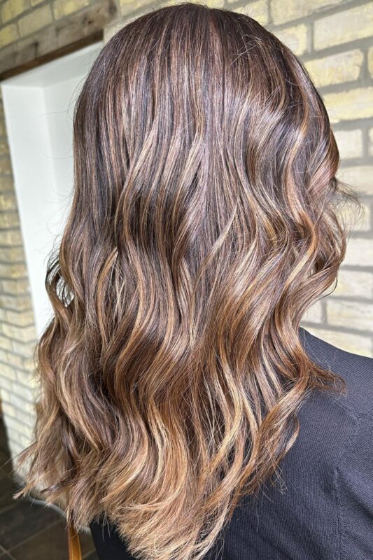 Mujer de cabello castaño oscuro y balayage caramelo.