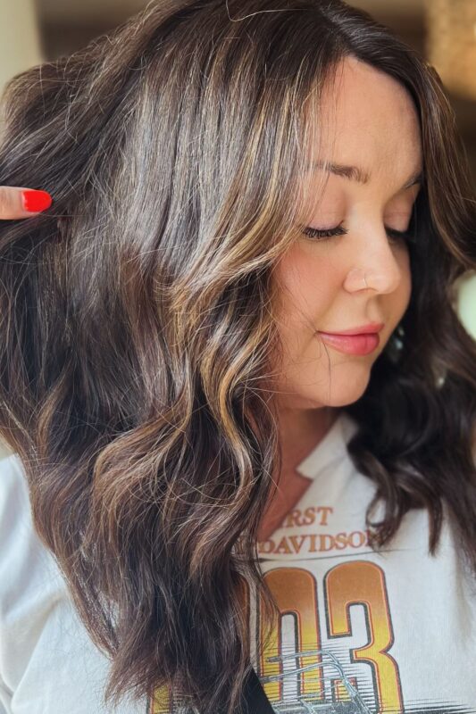 Mujer con cabello castaño chocolate profundo y balayage caramelo.