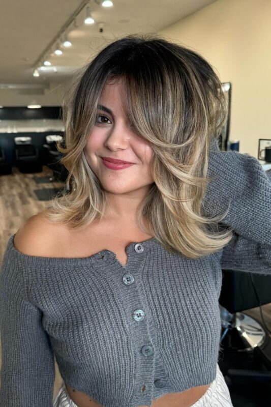 Mujer con balayage rubio brillante y vivido sobre cabello castaño oscuro.