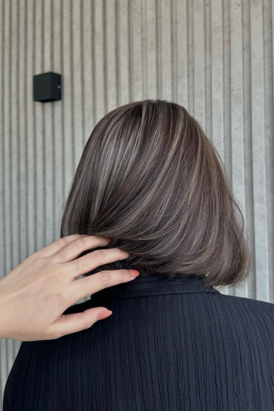 Woman with brown hair and highlights covering grey strands.