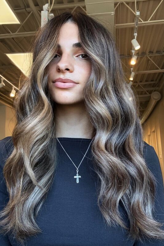 Woman with long sunlit balayage on a medium brown base.