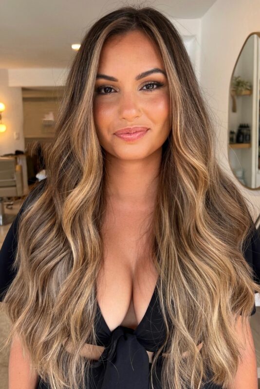 Woman with radiant honey blonde balayage on medium brown waves.