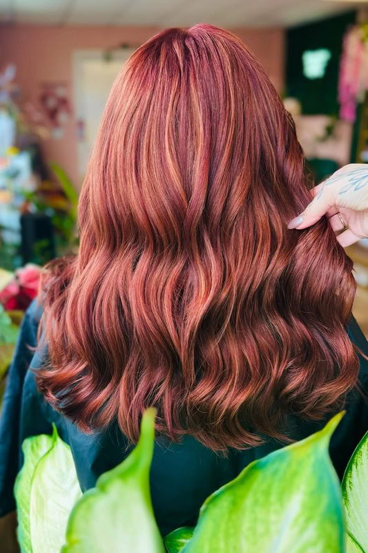 Woman with long wavy hair featuring red and brown highlights.