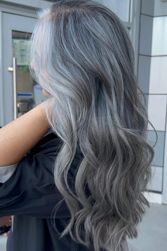 Woman with silver balayage on her dark hair and a silver money piece.