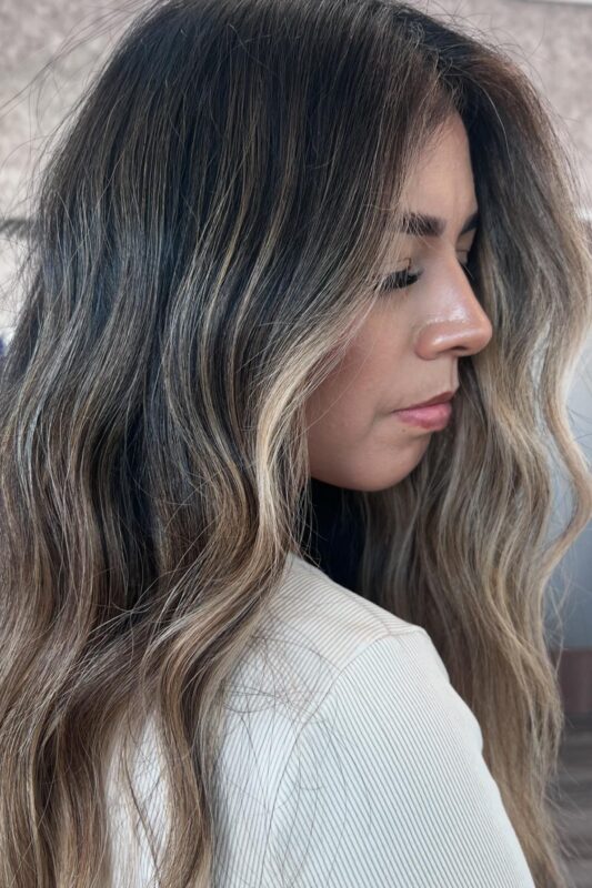 Mujer con balayage beige suave y ceniciento sobre cabello castaño medio.