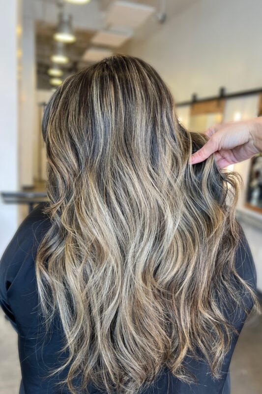 Mujer con balayage rubio miel dorado bañado por el sol y raíz derretida.