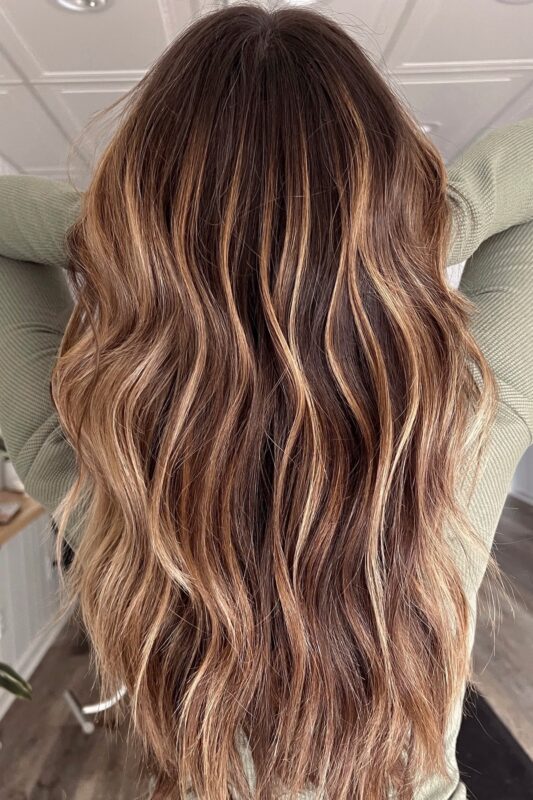 Mujer con balayage caramelo cálido sobre base marrón oscuro.