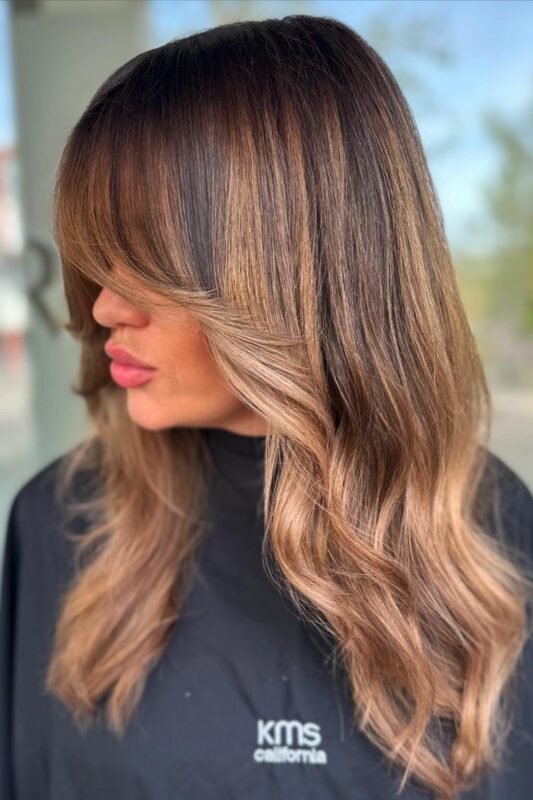 Mujer con balayage caramelo cálido sobre una base castaña oscura.