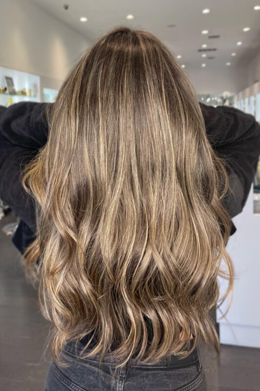 Mujer con cálido balayage rubio bañado por el sol sobre una base morena oscura.