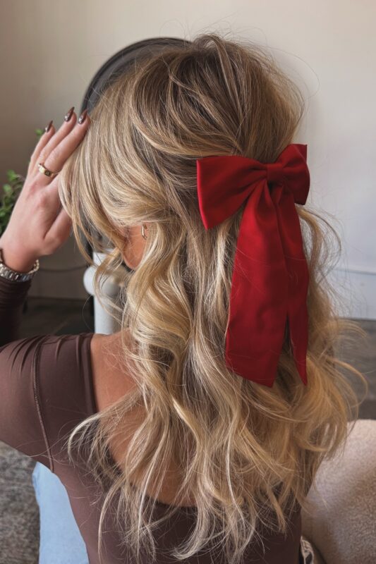 Woman with a half-up hairstyle featuring a classic red Christmas bow.