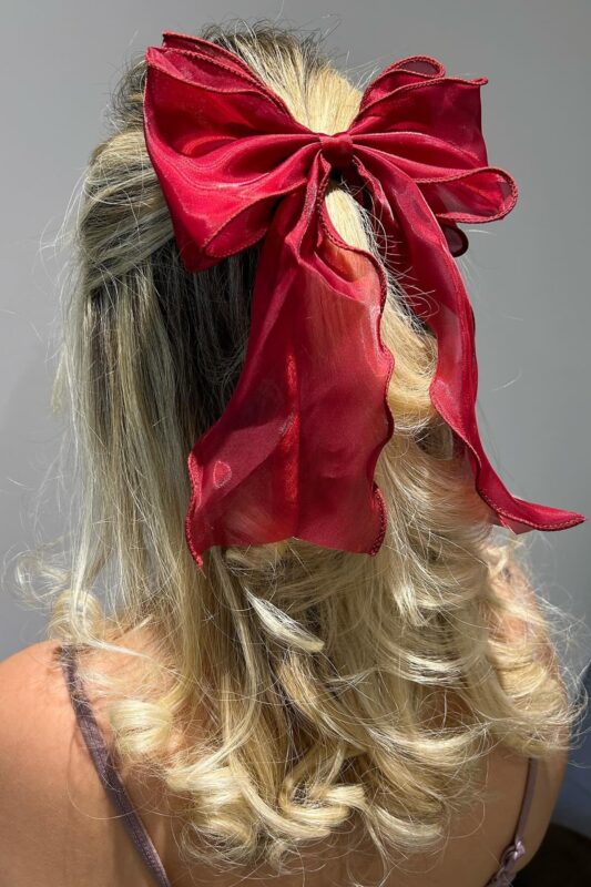 Woman with a half-up, half-down hairstyle adorned with a red ribbon bow.