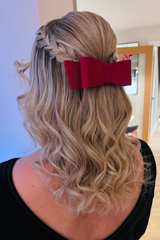 Woman with a half-up hairstyle featuring a side braid and a red bow.