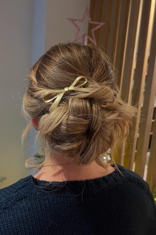 Woman with a braided updo adorned with a delicate golden ribbon bow.