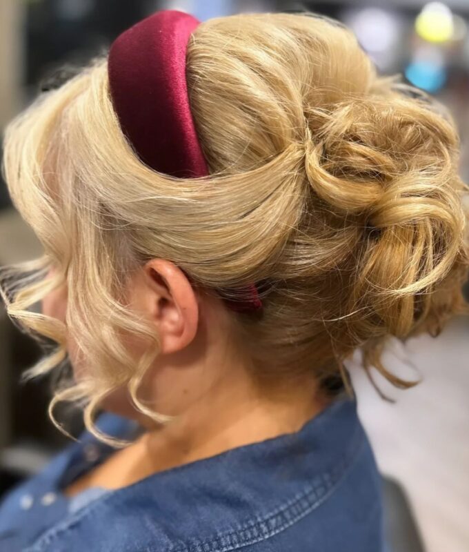 Woman with a messy updo bun styled with a burgundy velvet headband.