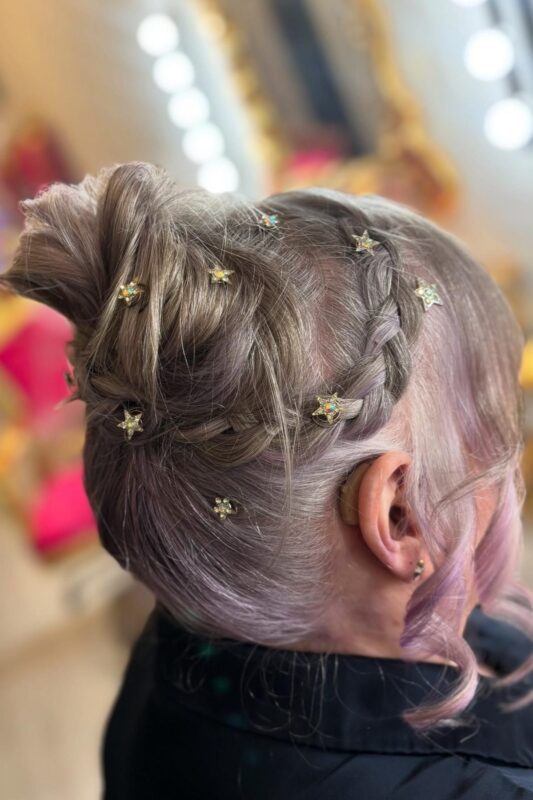 Woman with a messy updo featuring a side braid and star embellishments.