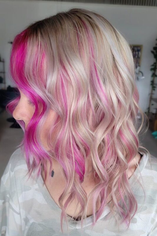 Woman with pink peekaboo highlights on her blonde hair.