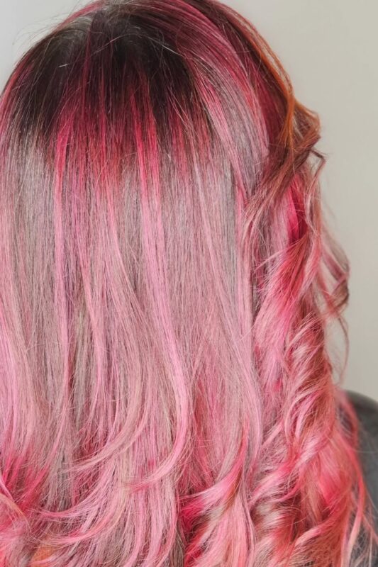 Woman with black hair featuring bold pink highlights and an orange money piece.