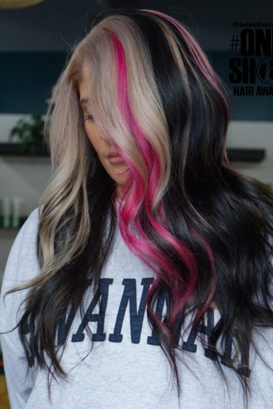 Woman with black and blonde color-blocked hair featuring a hot pink streak.