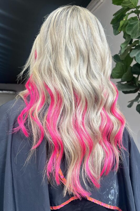 Woman with blonde hair featuring hot pink highlights.