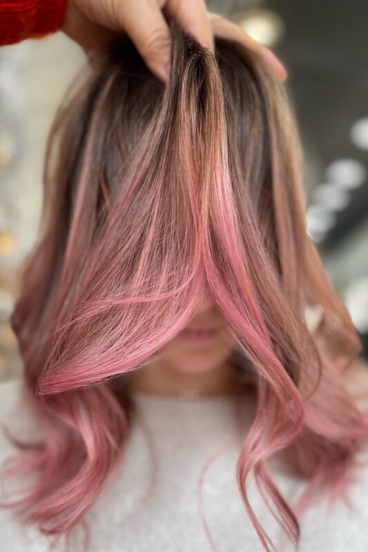 Woman with brown hair and rose gold pink highlights and money piece.