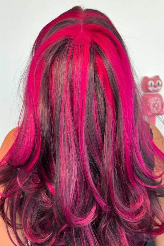 Woman with chunky hot pink highlights on a dark base.