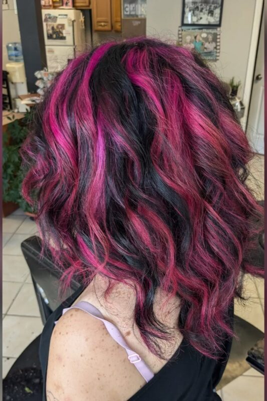 Woman with dark hair and hot pink streaks.