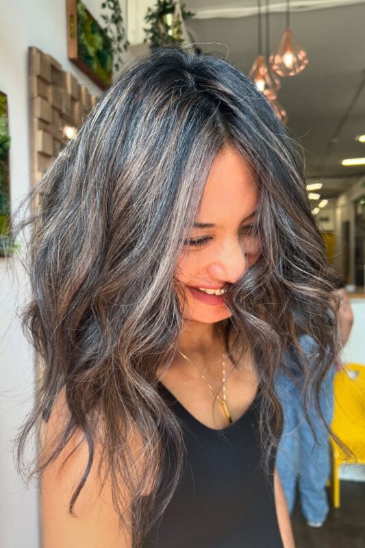 Gray blending balayage in dark hair with caramel highlights.