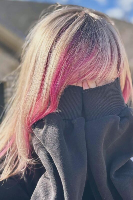 Woman with bright blonde hair featuring a pink money piece.