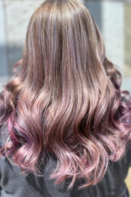 Woman with light brown hair featuring pink and purple peekaboos and platinum highlights.