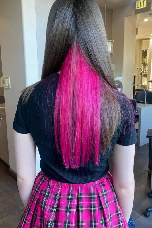 Woman with bright pink peekaboo highlights on her brown hair.