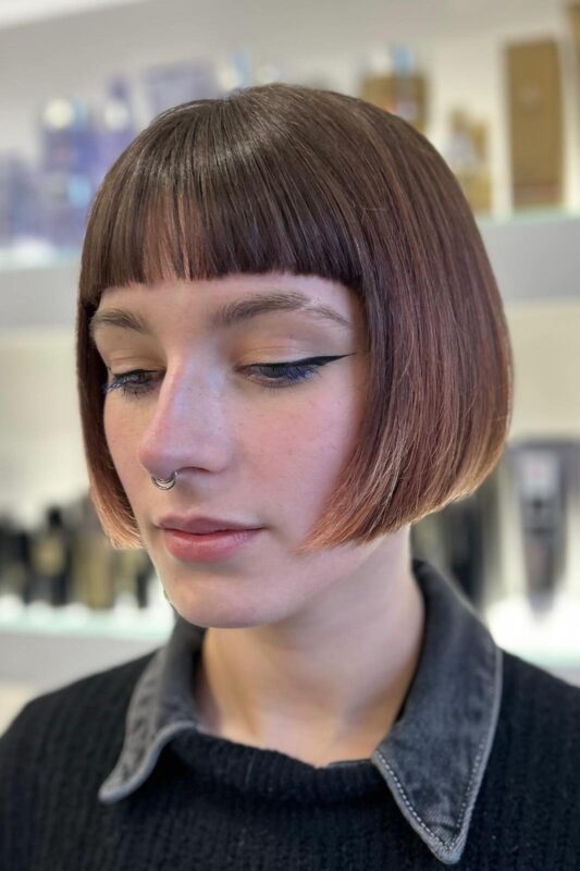 Woman with a short French bob haircut and blunt bangs.