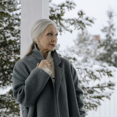 Older woman with beautiful gray hair standing outside in a gray coat.