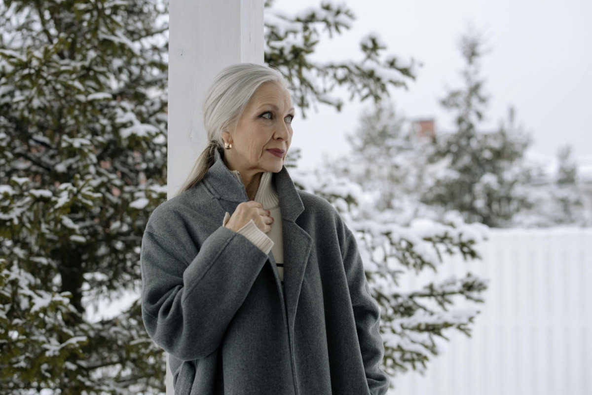 Older woman with beautiful gray hair standing outside in a gray coat.